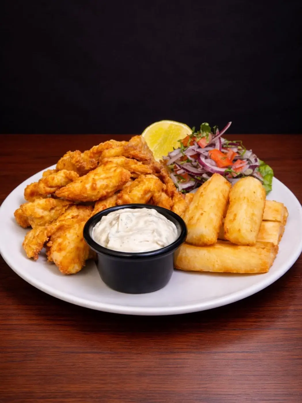 Fritura de pescado con yuca frita, ensalada de cebolla y salsa en un plato blanco
