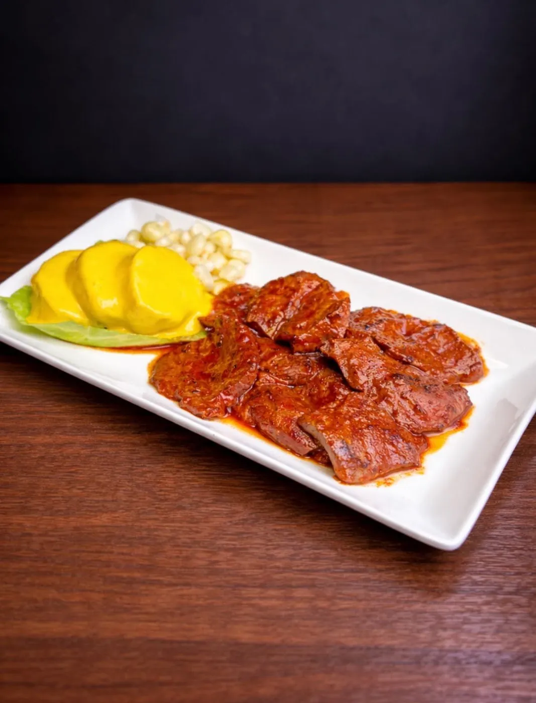 Lonchas de carne adobada con rodajas de patata y choclo en un plato blanco