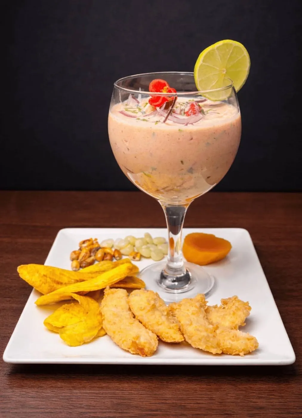 Copa de ceviche cremoso con fritura de pescado y plátano frito en un plato cuadrado