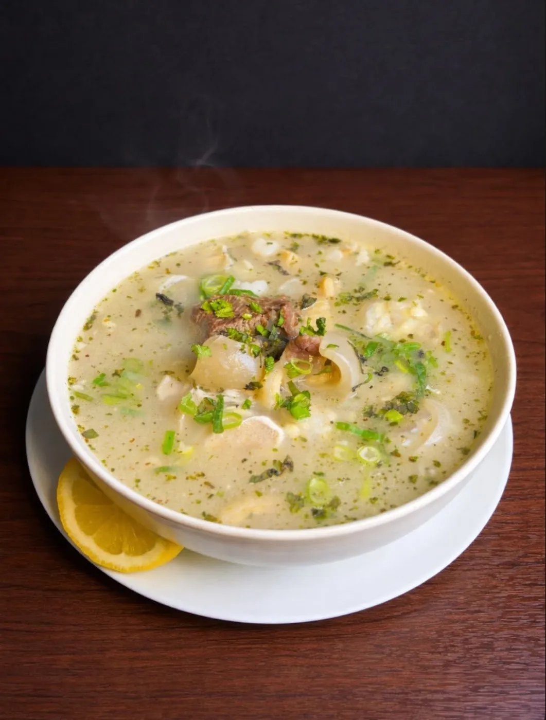 Sopa blanca con verduras y una rodaja de limón en un cuenco blanco