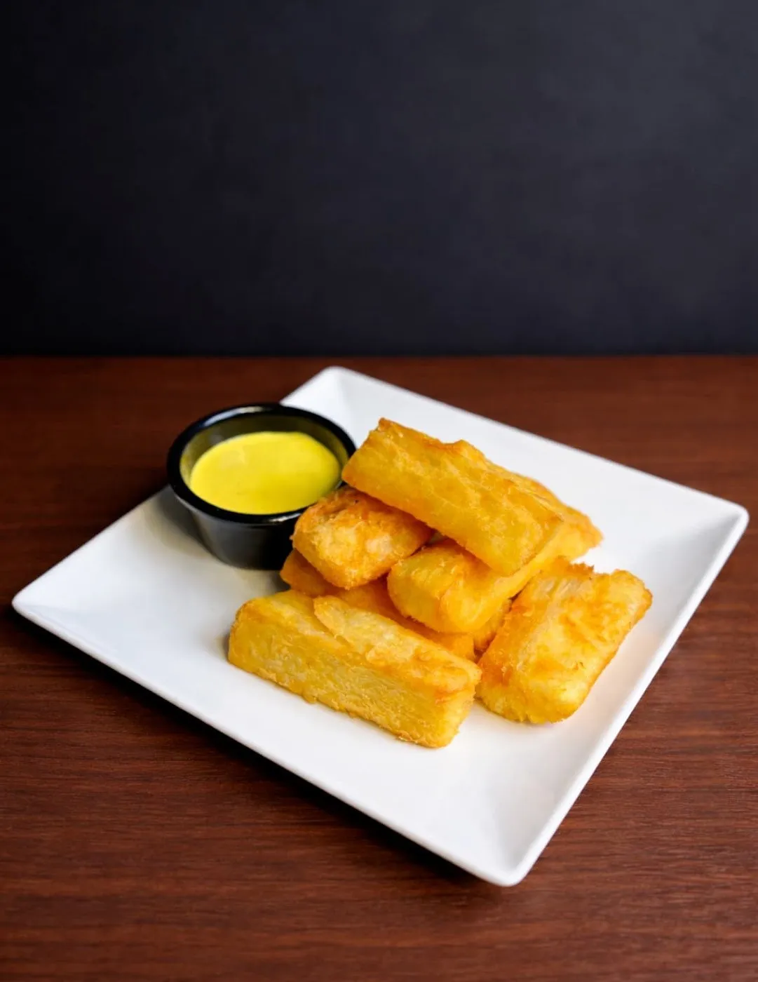 Yuca frita con una salsa amarilla en un plato cuadrado blanco