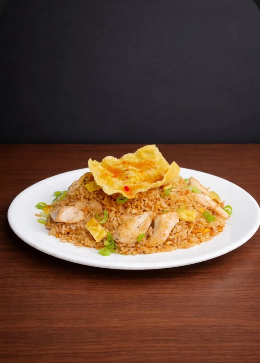 Arroz chaufa con pollo y una oblea frita por encima en un plato blanco