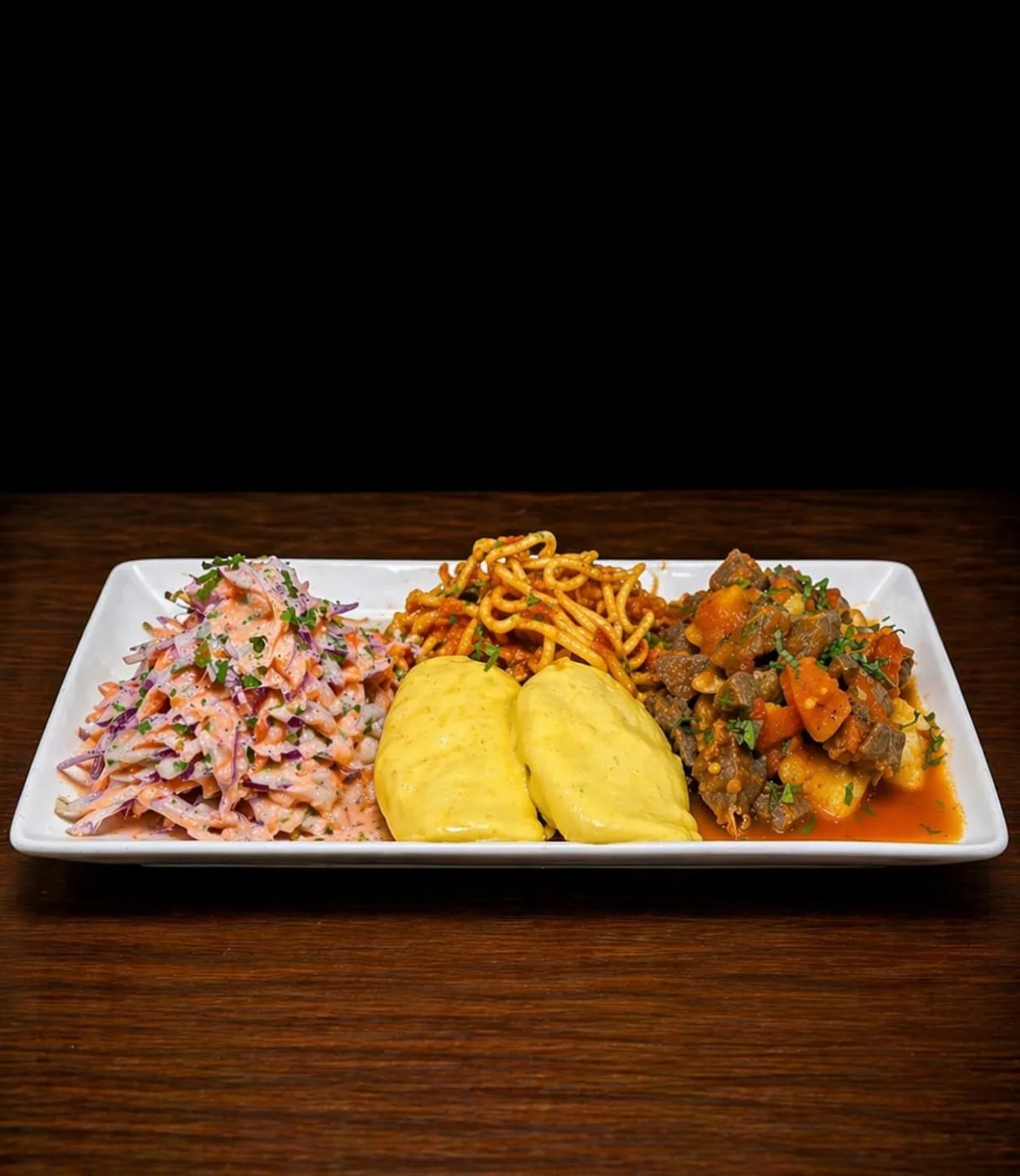Tres preparaciones en una fuente rectangular: ensalada, puré amarillo y guiso