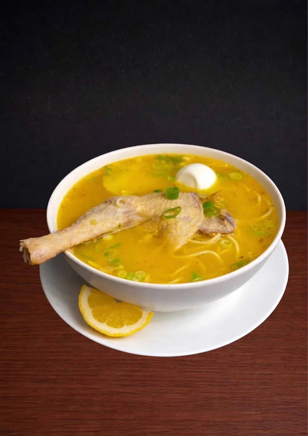 Caldo de gallina con fideos, huevo y limón en un cuenco blanco